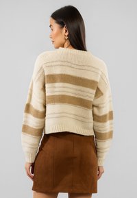 Maglione a righe crema e beige con design cropped, righe testurizzate e polsini a costine, abbinato a una minigonna in suede marrone.