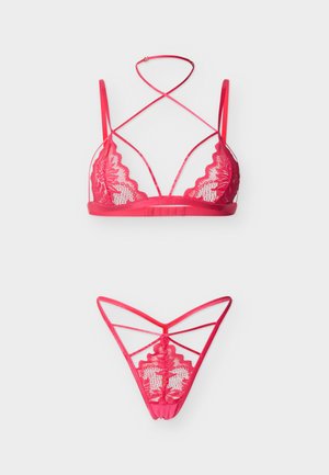 Raudonos nėriniuotos liemenėlės ir dirželių komplektas su gėlių raštais ir plonomis susikertančiomis petnešėlėmis ant balto fono.