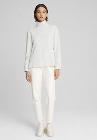 Top gris claro de cuello alto con mangas largas, combinado con pantalones blancos ajustados. La tela parece suave y ligeramente texturizada, adecuada para uso casual.