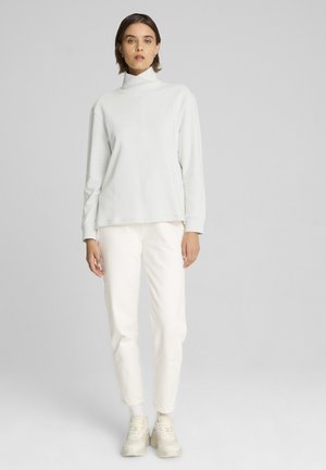 Top gris claro de cuello alto con mangas largas, combinado con pantalones blancos ajustados. La tela parece suave y ligeramente texturizada, adecuada para uso casual.