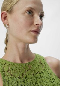 Top de encaje verde con patrones florales, diseño sin mangas, cuello redondo, con detalles intrincados y un acabado texturizado.