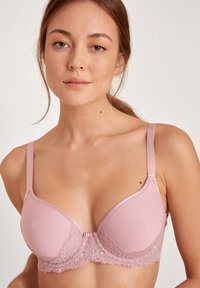 Lichtroze beha met gladde, gevormde cups en kantdetails bij de onderband. Verstelbare banden en een haak-en-oogsluiting aan de achterkant.