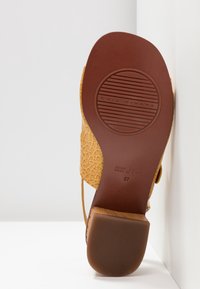 Sandale en cuir jaune avec une tige texturée à motif crocodile, et une semelle brune lisse présentant un design circulaire et un logo.