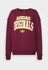 Vinröd sweatshirt i bomullsblandning med fet vit och gul text "ADIDAS ORIGINALS". Långa ärmar och ribbade muddar.