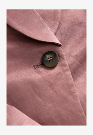 Blazer in lino rosa con una texture liscia, rever appuntiti e un bottone scuro e testurizzato con quattro fori.