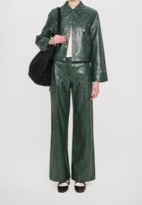 Zielona, pomarszczona skórzana kurtka i pasujące szerokie spodnie, zestawione z czarną plecioną torbą typu tote oraz brązowymi płaskimi butami z białymi akcentami.