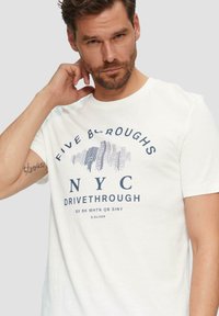 Witte katoenen t-shirt met korte mouwen, met een marineblauwe grafische print die "FIVE BOROUGHS NYC DRIVETHROUGH" en een gestileerd stadsprofiel bevat.
