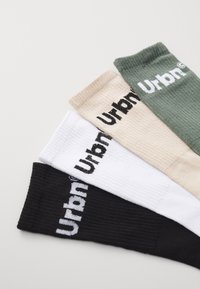 Cuatro pares de calcetines acanalados en negro, blanco, beige y verde, cada uno con la palabra "Urbano" bordada en contraste.