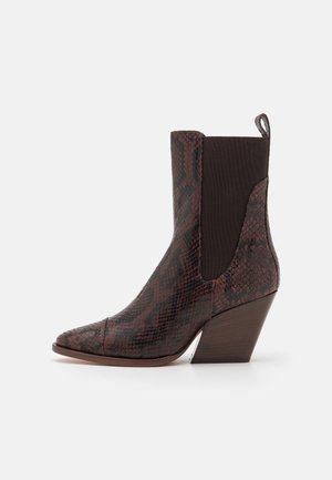 Brązowe botki ankle w wężowy wzór z długim noskiem, elastycznymi bocznymi panelami i ciemnym, drewnianym obcasem. Teksturowany wzór węża pokrywa całe buty.