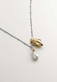 Collar que presenta una cadena de plata, un charm dorado con forma de concha y una perla blanca colgante. Son visibles acentos en plata y oro.