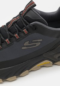 Black hiking shoe with textured mesh and synthetic overlays. Features red and beige laces and a Goodyear rubber outsole for traction.