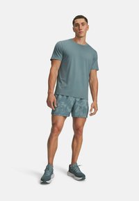 Conjunto deportivo que incluye una camiseta de manga corta en color verde azulado, pantalones cortos estampados y zapatillas verdes azules. La tela es suave y transpirable.