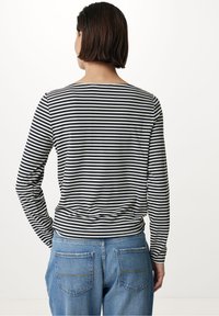 Svart- och vitrandig långärmad topp med rund halsringning, kombinerad med ljusblå denimjeans. Toppens passform är avslappnad.