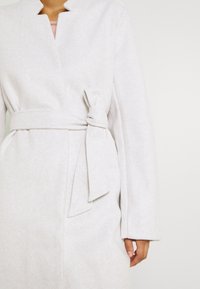 Jasnoszary płaszcz o gładkiej fakturze, z paskiem do wiązania w talii i bez kołnierza. Długie rękawy i minimalistyczny styl.