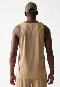 Μπεζ αμάνικη φανέλα από δίχτυ με χαλαρή εφαρμογή, με στρογγυλή λαιμόκοψη και φαρδιά μανικάκια. Φορεμένη με ταιριαστό σορτς, από την πίσω όψη.