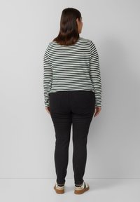 Gestreepte langmouwtop in groen en wit, gecombineerd met zwarte broek. De top heeft een ronde halslijn en een getailleerde pasvorm, terwijl de broek slim-fit is.