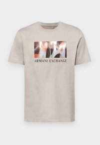 Béžové tričko Armani Exchange s krátkým rukávem, kulatým výstřihem a barevným kovovým logem "AX Armani Exchange" na hrudi.