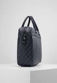 Sac à main en cuir bleu marine avec une finition texturée, deux poignées, une fermeture éclair sur le dessus et un motif de logo en relief subtil sur la surface.