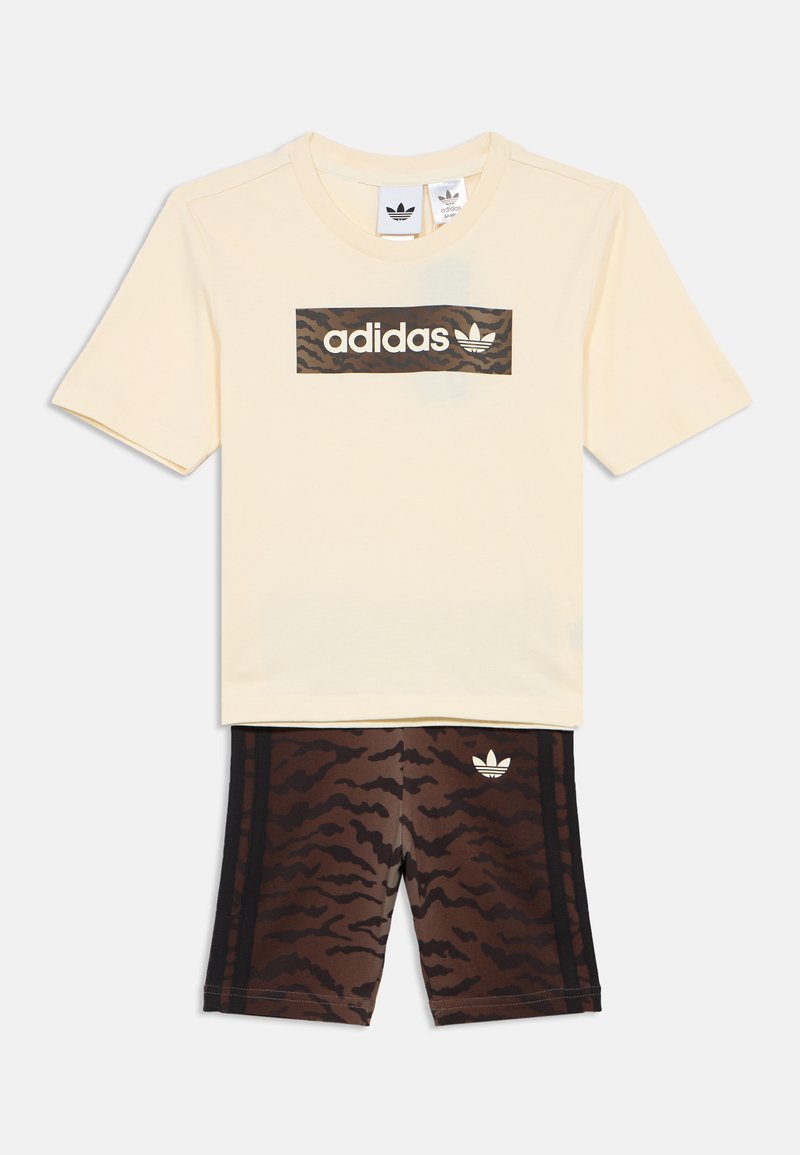 Zestaw dziecięcy Adidas składający się z beżowej koszulki z kamuflażowym logo oraz brązowych spodni krótkich z wzorem i czarnymi bocznymi paskami.