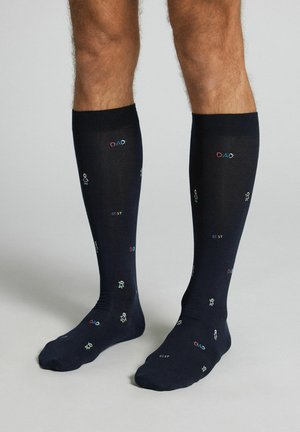 Beine mit schwarzen knielangen Socken, verziert mit bunten kleinen Strichmännchen und den Worten "DAD" und "BEST" als wiederholtes Muster.