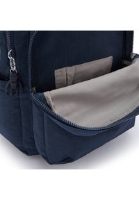 Sac à dos bleu marine avec une poche à fermeture éclair à l'avant, doté d'un intérieur gris clair et d'un tirette en forme de singe en caoutchouc. Texture de tissu lisse.