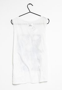 Vit ärmlös t-shirt i lätt tyg, med rund halsringning och ett subtilt, blekt tryck över framsidan. Hänger på en svart krok.