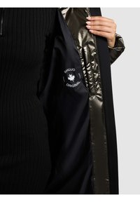 Melna jaka ar spīdīgu, tumšu oderi. Ārējai kārtai raksturīga ribaina tekstūra, uz iekšējā auduma atrodas logotips. Aizdare ar rāvējslēdzēju.