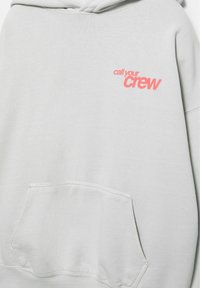 Svetlosivá mikina s kapucňou a predným vreckom, s červeným textom "call your crew" potlačeným na ľavej strane hrudníka.
