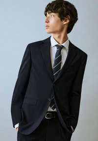 Crni sako sa jednim dugmetom, bijela košulja i crna kravata s svijetloplavim prugama. Glatka tkanina i kroj po mjeri.