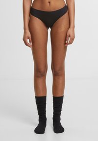 Musthave musta bikiinialuspesu, millel on sile tekstuur ja mõõdukas katvus, koos mustade, kokku ruuditatud kudumite sokkidega.