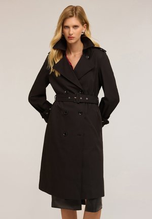 Manteau noir en trench avec des boutons à double boutonnage, des larges revers, une taille ceinturée et des épaulettes, présentant un tissu lisse et texturé.