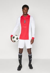 Sarkana un balta garo piedurkņu futbola krekls ar apkakli, ar emblēmu un tekstu "Eggo". Valkā ar baltām šortiem, melnām zeķēm un futbola apaviem.