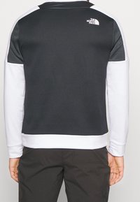 Pullover a maniche lunghe bianco e nero con un retro nero testurizzato e maniche bianche lisce; presenta il logo del marchio sulla parte superiore del retro.