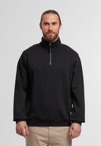 Felpa nera a maniche lunghe con colletto alto e mezzo zip. Realizzata in un materiale morbido, presenta una vestibilità rilassata e polsini a costine.