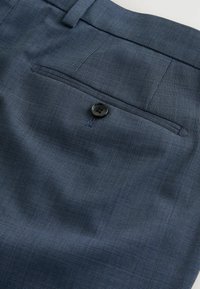 Poche arrière d'un pantalon de costume bleu foncé texturé avec une fermeture à bouton noir unique.