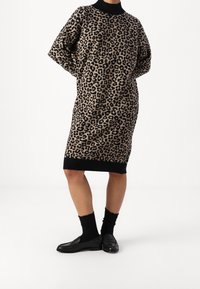 Leopardmönstrad klänning i beige och svart, med ribbat halsudds, korta ärmar och en löst sittande passform. Matchas med svarta loafers och strumpor.