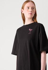 Black cotton t-shirt with a relaxed fit, short sleeves, and a pink embroidered cocktail glass design on the chest.