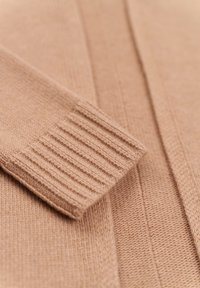 Beige knit cardigan with ribbed cuffs, featuring a textured pattern and smooth finish. Close-up view highlights fabric detail and design.