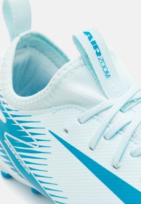 Botín de fútbol azul claro con parte superior texturizada, rayas azules prominentes y una pestaña en bucle. El diseño incluye una etiqueta de marca "AIR ZOOM".