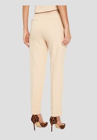 Beige tailored pants with a straight leg cut, featuring two back pockets, paired with leopard print high heels. Smooth fabric texture.