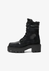 Schwarze Schnürstiefelette mit einem Obermaterial aus Wildleder, glänzenden Lederelementen, dicker Plateau-Sohle und einem mit Lammwolle gefütterten Kragen.
