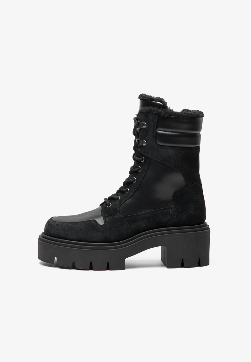 Schwarze Schnürstiefelette mit einem Obermaterial aus Wildleder, glänzenden Lederelementen, dicker Plateau-Sohle und einem mit Lammwolle gefütterten Kragen.