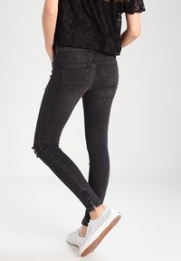 Jeans negros ajustados con dobladillos deshilachados, diseño de cinco bolsillos y cintura a media altura. Llevados con una blusa de encaje negra y zapatillas blancas.
