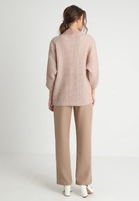 Jasnoróżowy dzianinowy sweter z fakturowanym, prążkowanym wzorem, w zestawieniu z beżowymi szerokimi spodniami i białymi butami na obcasie.