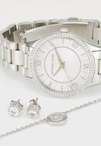 Zilveren Michael Kors horloge met kristallen rand, bijpassende kristallen oorknopjes en een zilveren kettingarmband met ronde kristallen hanger.