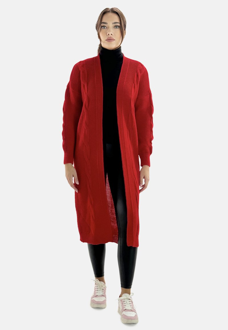 Röd stickad kofta med flätstickat mönster, långa ärmar, öppen front, bärs över en svart polotröja och kombineras med svarta leggings och sneakers.