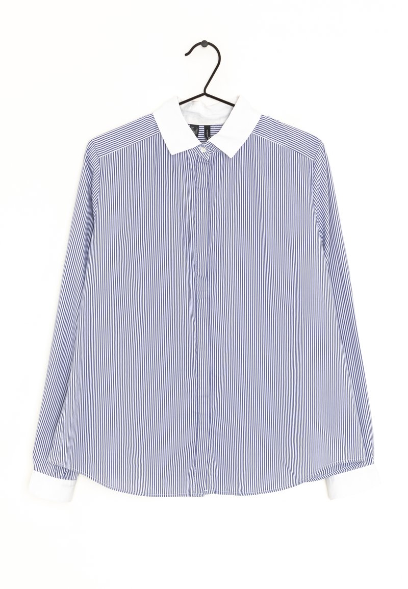 Chemise à rayures verticales bleues et blanches à manches longues avec col et poignets blancs suspendue à un cintre noir sur fond blanc.