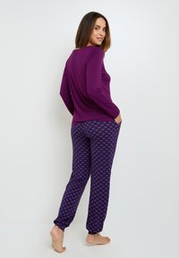 Un haut violet à manches longues associé à un pantalon de pyjama violet à motifs avec de petits dessins, fabriqué en tissu doux et avec une coupe décontractée.