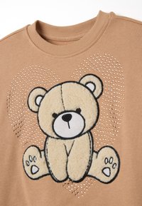 Beige sweatshirt met een berenontwerp met een pluizige textuur, omringd door rhinestones in een hartpatroon, en een geribde ronde hals.