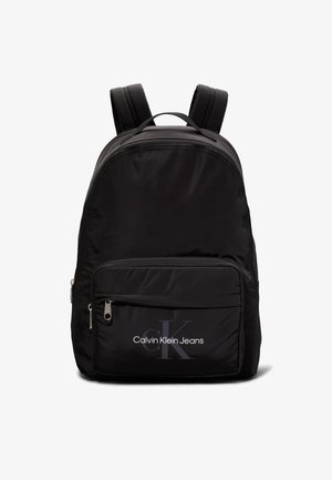 Mustmust must-seljakott, millel on reguleeritavad rihmad, eesmine lukuga tasku ja "Calvin Klein Jeans" logo trükitud esiküljel.